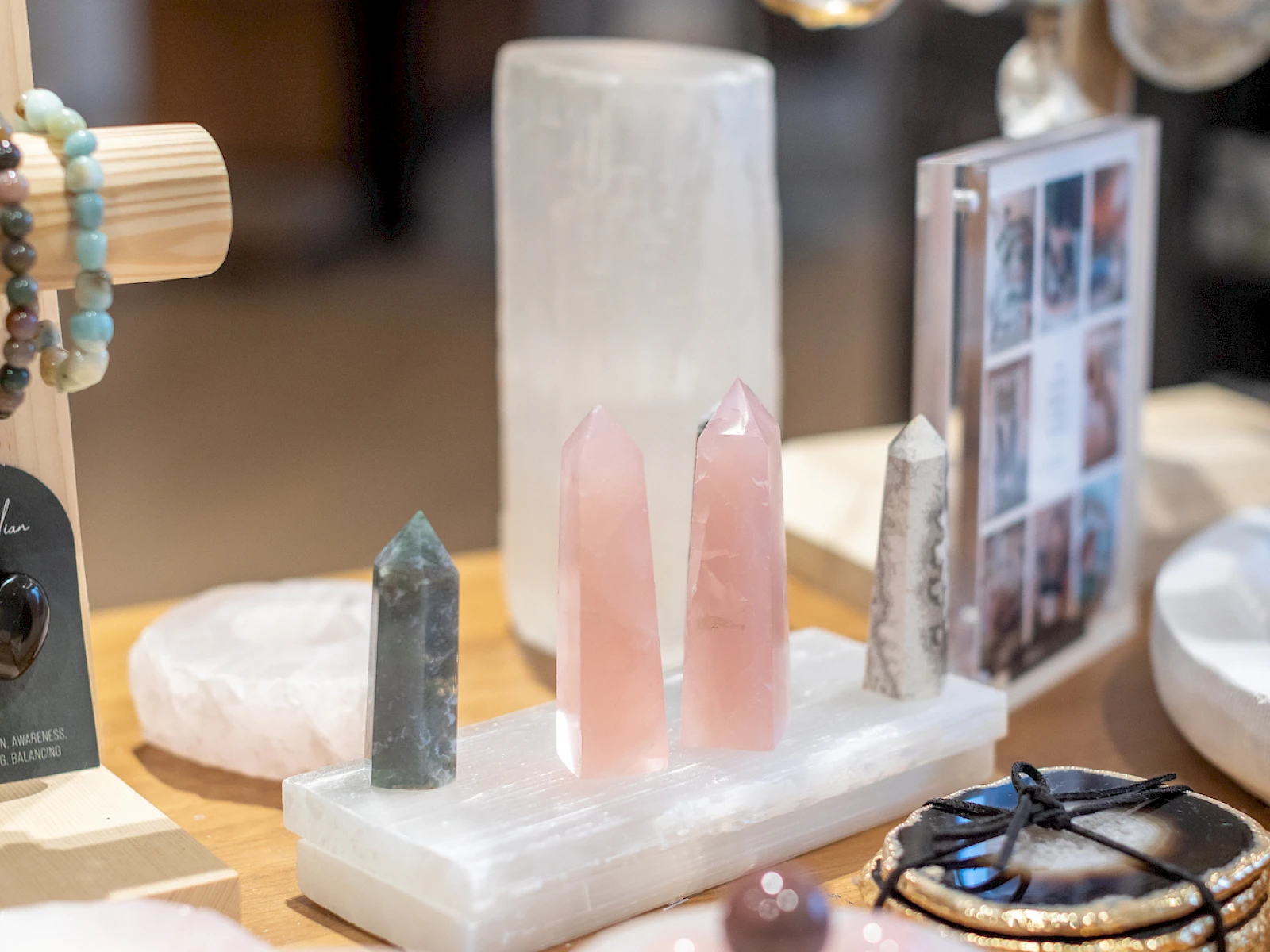 A small display of crystal towers and pink stones on a white base, with bracelets and hanging jewelry in the background, and photos nearby.