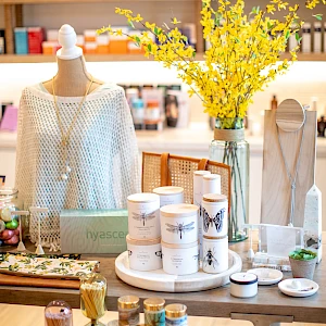 A chic boutique display featuring skincare jars, a white knit sweater on a mannequin, yellow flowers, and shelves of colorful products in the background.