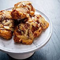 Delicious almond-topped pastries stacked on a small white pedestal, golden-brown and crunchy, perfect for a sweet tea time treat.