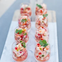 A tray of colorful shrimp cocktails or shrimp skewers arranged in small glasses, garnished with herbs and diced vegetables, ready to serve.