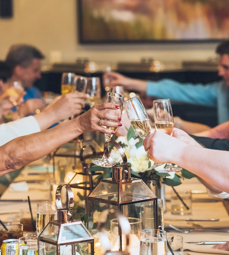 A group of people toasting with wine glasses at a candlelit dinner table with flowers and decorative lanterns.
