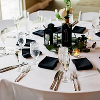 A round table set for a formal event with white tablecloths, glassware, silverware, black napkins, candles, and a centerpiece; elegant dining setup.