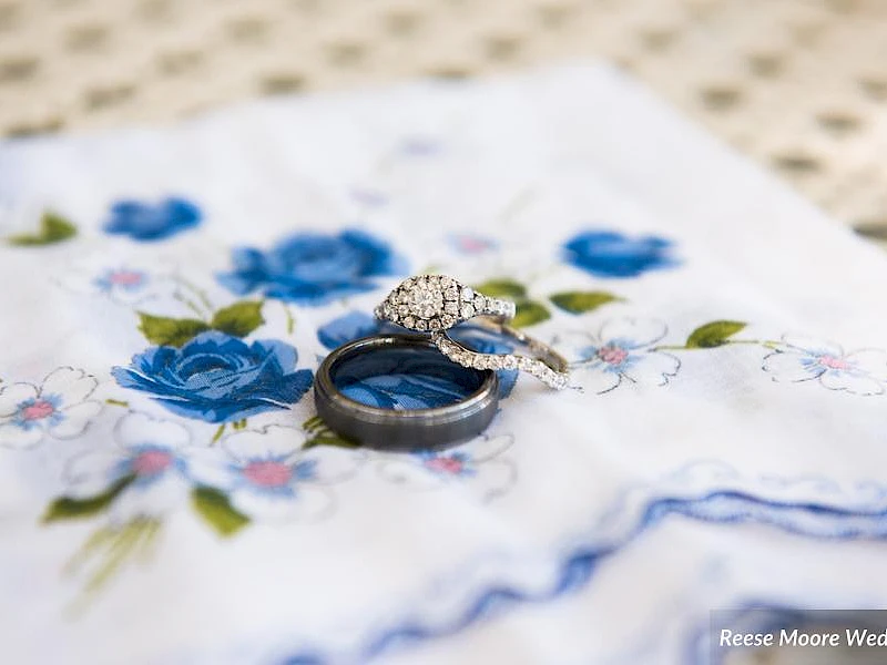 A pair of wedding rings on a floral cloth, one diamond-encrusted, resting atop a delicate blue-and-white fabric for a wedding moment.