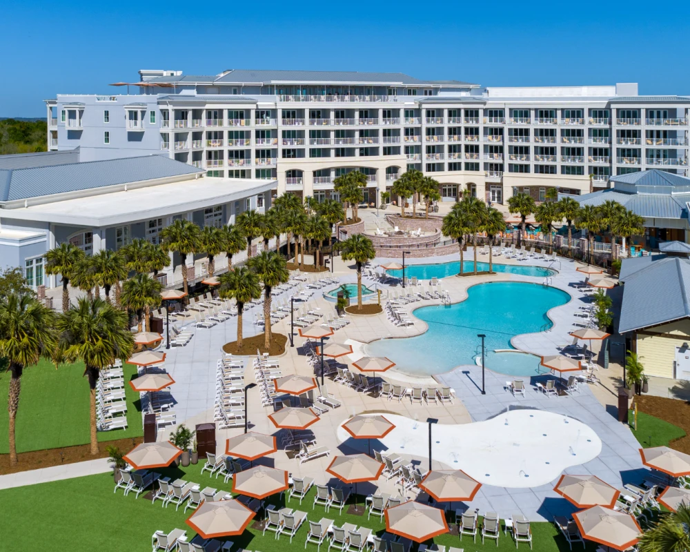 A sunny resort pool area with lounge chairs, palm trees, and a large white hotel building in the background, under a clear blue sky, nice and inviting.