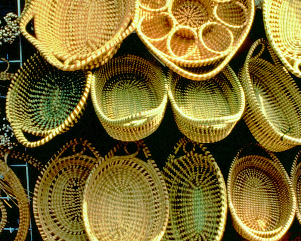 Handwoven bamboo baskets for sale, oval and round, natural tan color, intricate weave patterns, stacked on shelves for display.