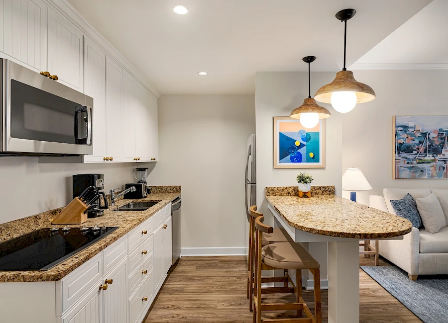 A modern kitchen with white cabinets, granite countertops, stainless steel appliances, and a breakfast bar that opens to a living area.