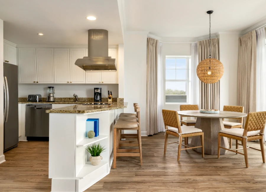 A bright open-concept kitchen and dining area with white cabinets, stainless appliances, a center island, and a cozy round dining set under a woven pendant light.