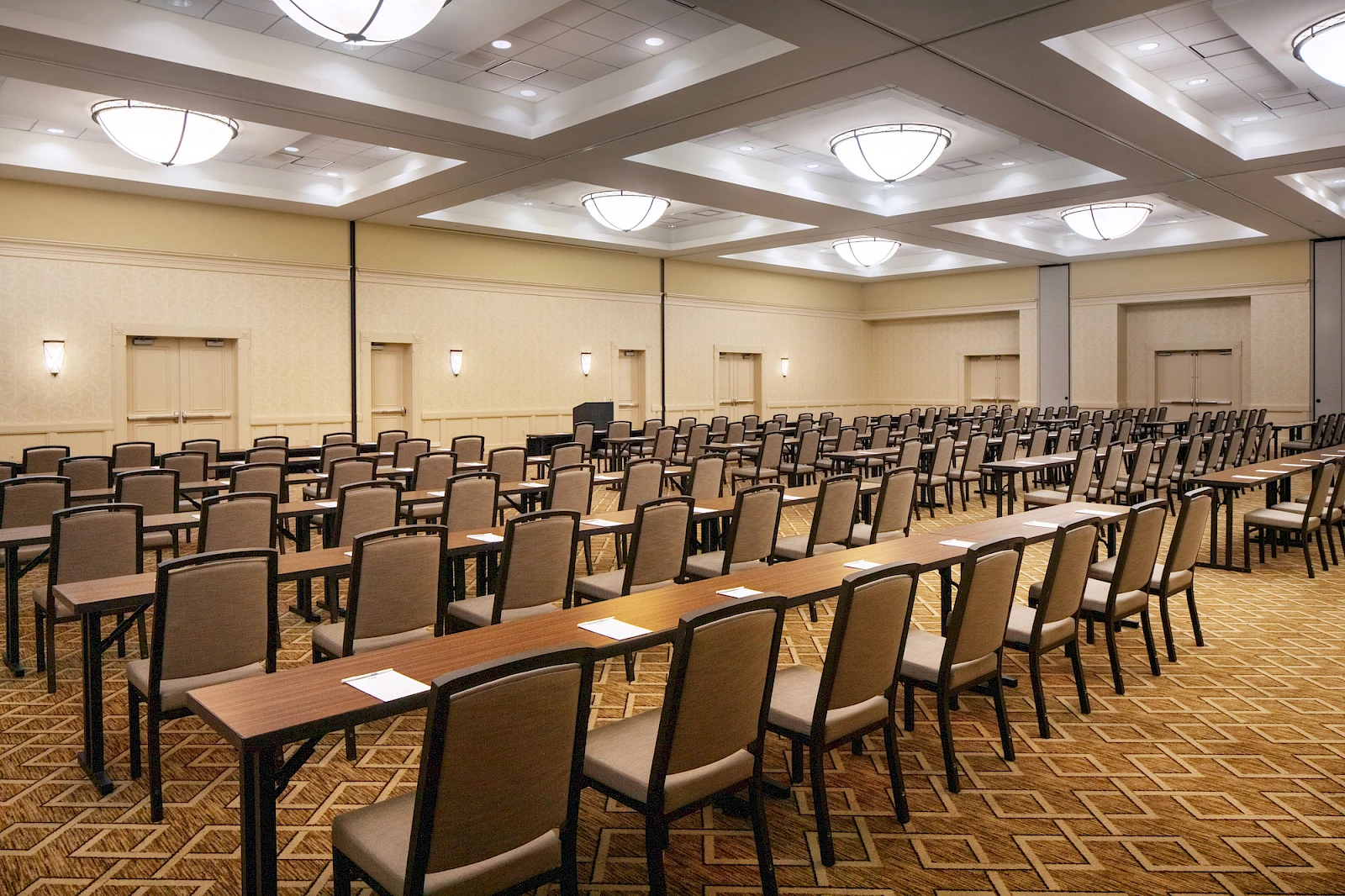 A large conference room set up with many rows of chairs and long tables, arranged theater-style for a presentation or meeting, neutral lighting.