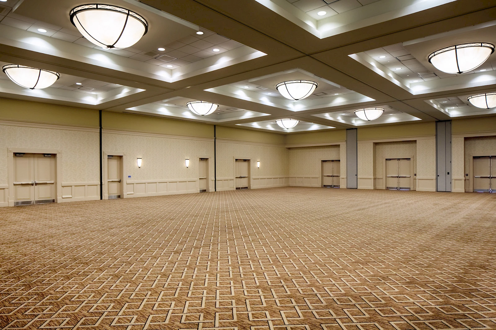 A large empty conference room with patterned carpet, beige walls, and multiple ceiling lights in a spacious ballroom.