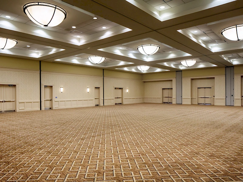 A large empty conference room with patterned carpet, beige walls, and multiple ceiling lights in a spacious ballroom.