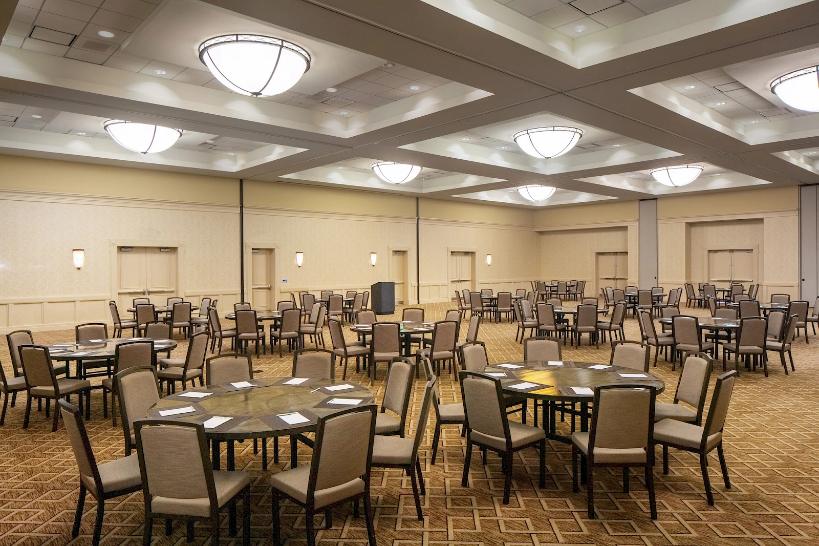 A spacious banquet hall set for a formal event with multiple round tables, chairs, and place settings, ready for dining and mingling.