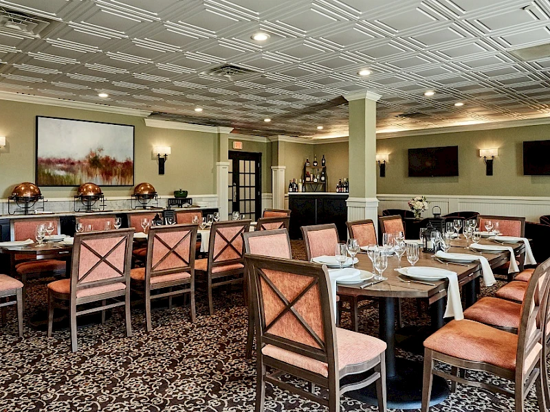 A formal dining room with wood chairs, pinkish cushions, arranged tables, place settings, and soft wall lighting—elegant and inviting.