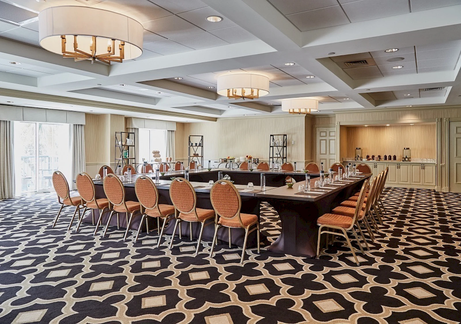A large conference room with a U-shaped table setup, orange chairs, decorative lighting, and a patterned carpet. The space appears ready for a meeting or event.