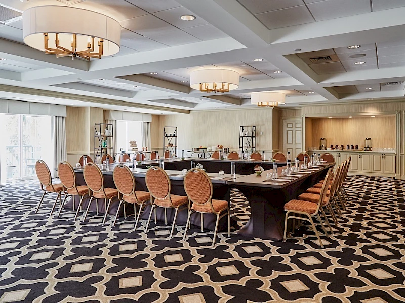 A large conference room with a U-shaped table setup, orange chairs, decorative lighting, and a patterned carpet. The space appears ready for a meeting or event.