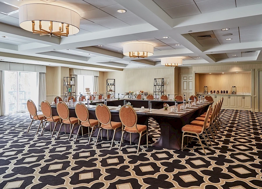 A large conference room with a U-shaped table setup, orange chairs, decorative lighting, and a patterned carpet. The space appears ready for a meeting or event.