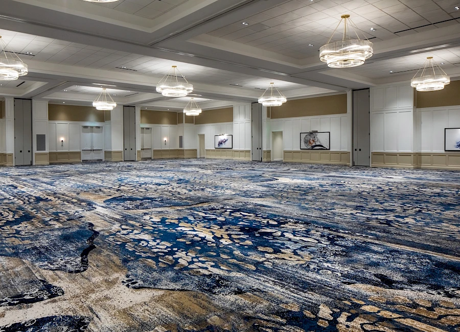 A large empty conference hall with patterned blue-carpet, high ceilings, and hanging chandelier lights, ready for an event.
