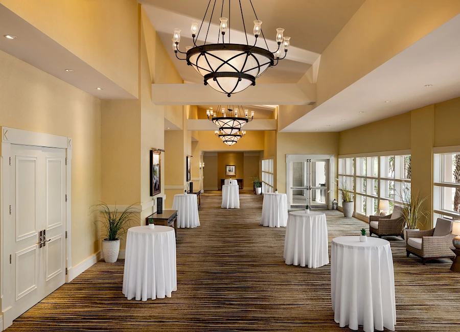 A spacious event hall with high ceilings, warm lighting, and tall cocktail tables draped in white linens, ready for a reception.