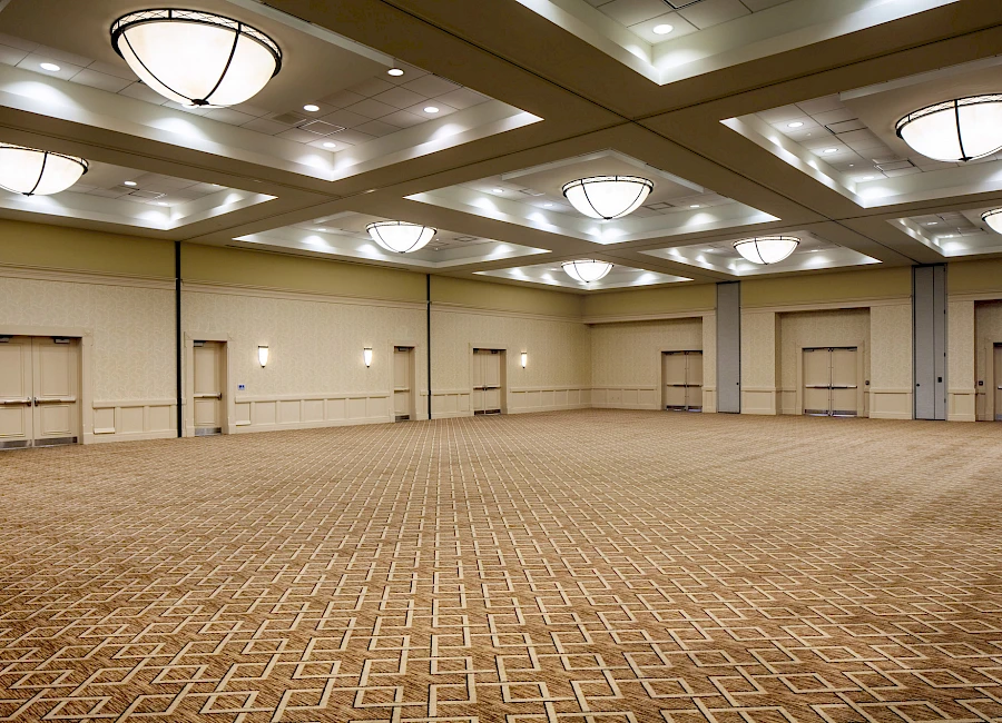 A vast, empty conference hall with patterned carpet, beige walls, and multiple ceiling lights—no furniture or people in sight, spacious and blank.
