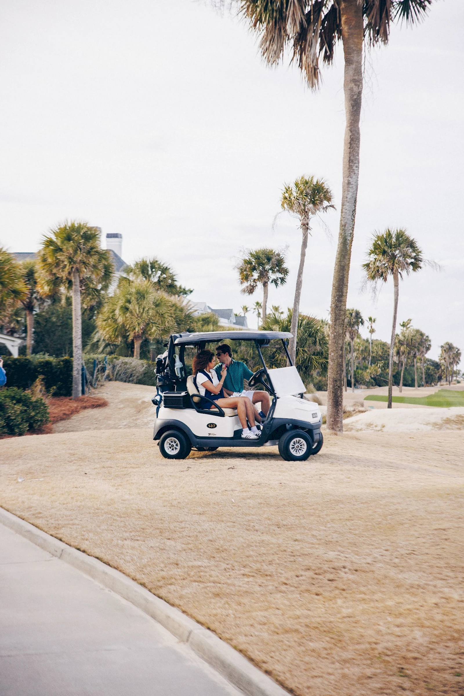 A sunny scene with a small golf cart carrying several people along a palm-lined path near a coastal area, leisure vibe and bright day.