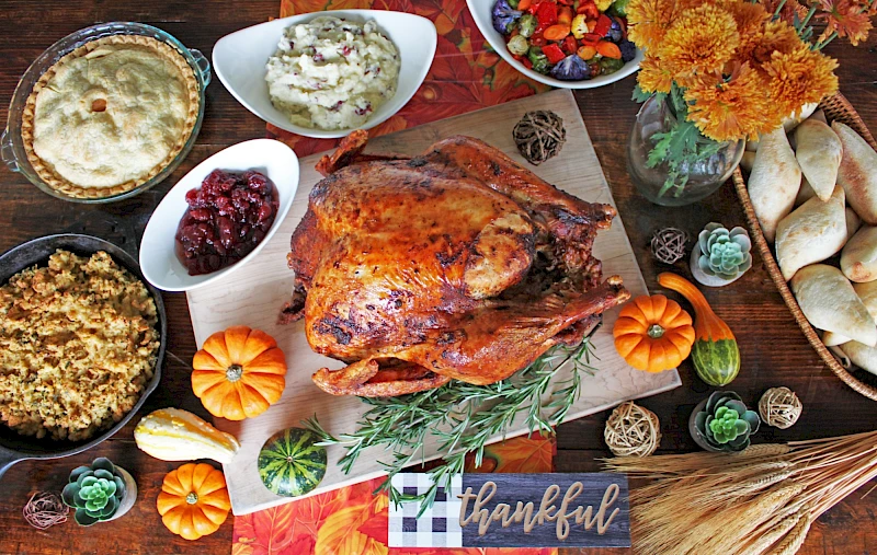 A roasted turkey centerpiece surrounded by sides, breads, pumpkins, herbs, and autumn décor on a festive table.