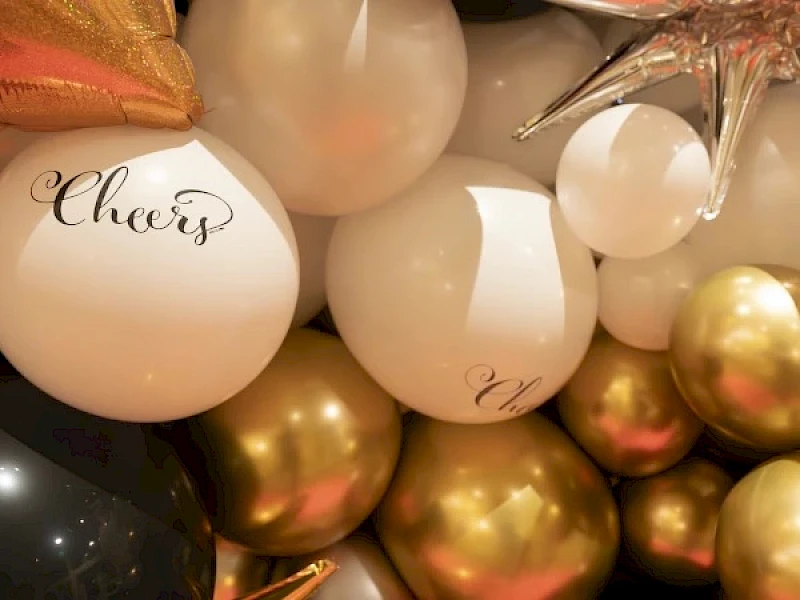 A festive cluster of white, gold, and rose balloons with cursive “Cheers” text, creating a celebratory party vibe.