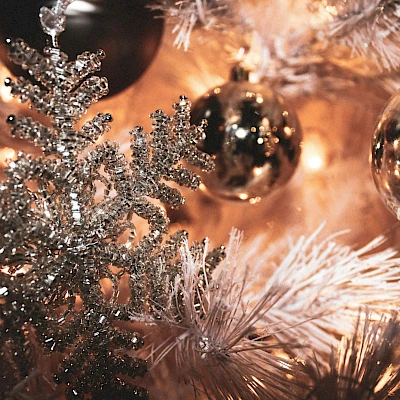Sparkling silver and white Christmas decorations on a tree, with glittery frosted branches and shiny ornaments, warm festive lights, and a cozy glow.