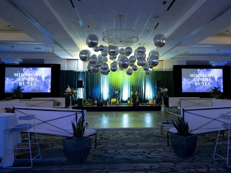 A conference or event stage with blue lighting, screens reading “MISSING DUNES,” podiums, and decorative orbs overhead in a formal venue. Yes.
