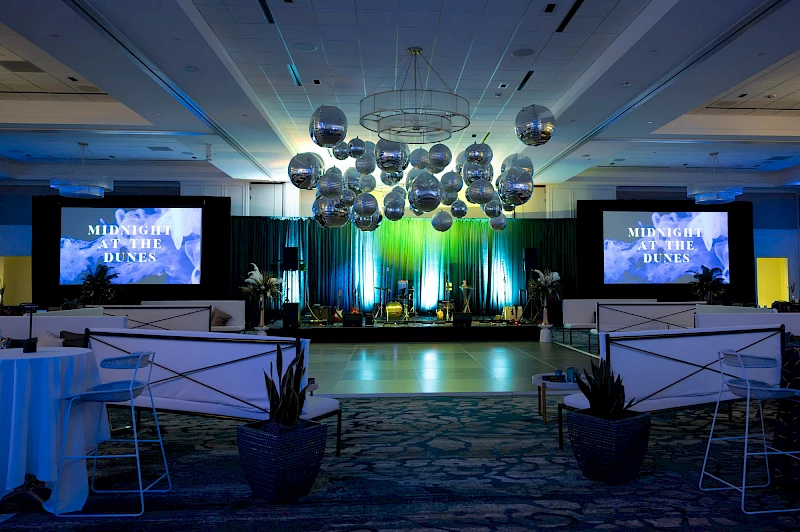 A conference or event stage with blue lighting, screens reading “MISSING DUNES,” podiums, and decorative orbs overhead in a formal venue. Yes.