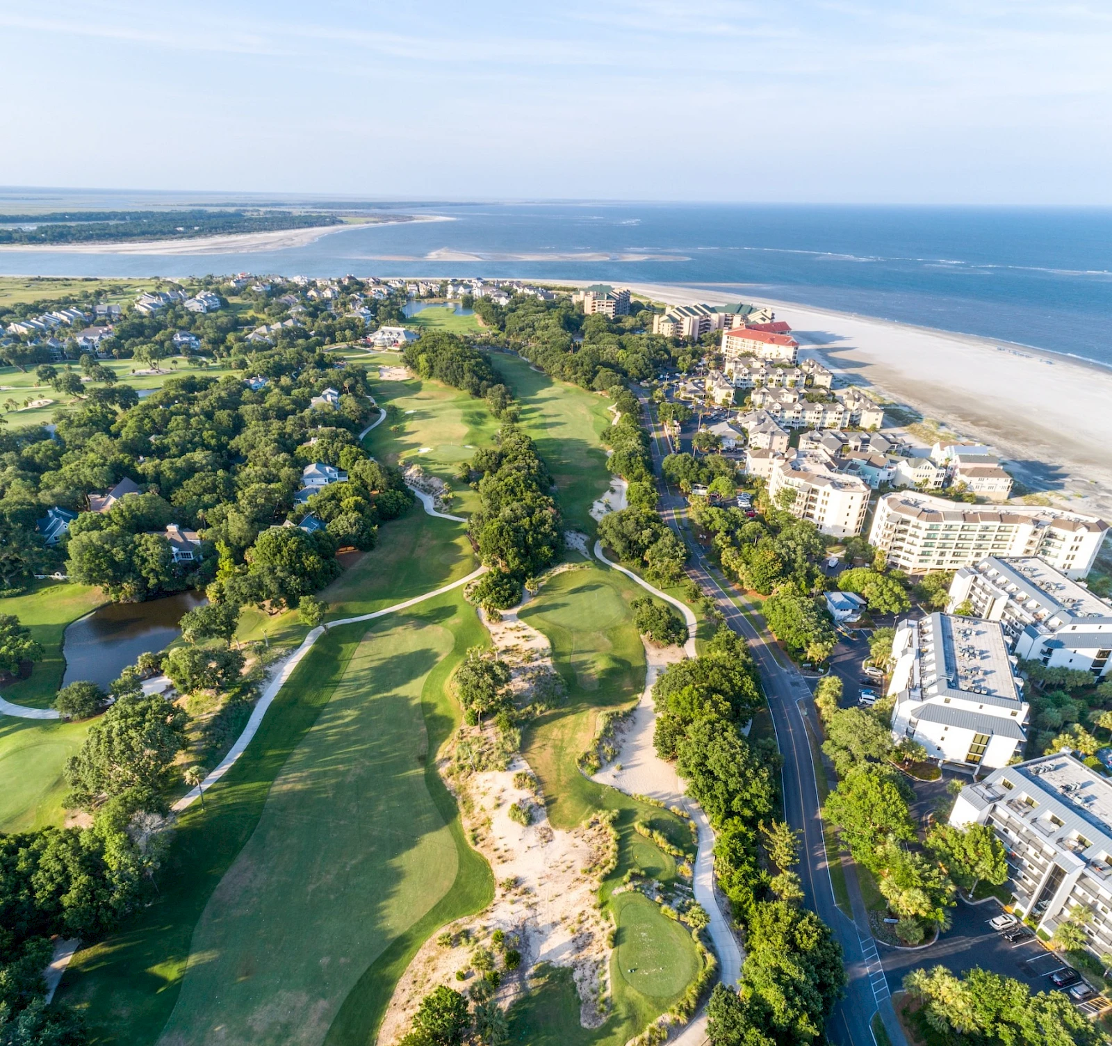 Aerial view of a coastal resort with sandy beaches, lush green golf courses, and resort buildings lining the shore, blending seaside relaxation with greens.