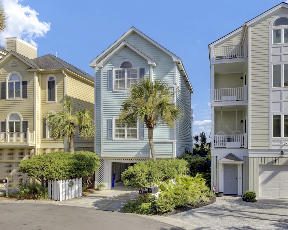 Colorful coastal townhouses with palm trees, garages, and balconies on a sunny day, lined up along a quiet street.