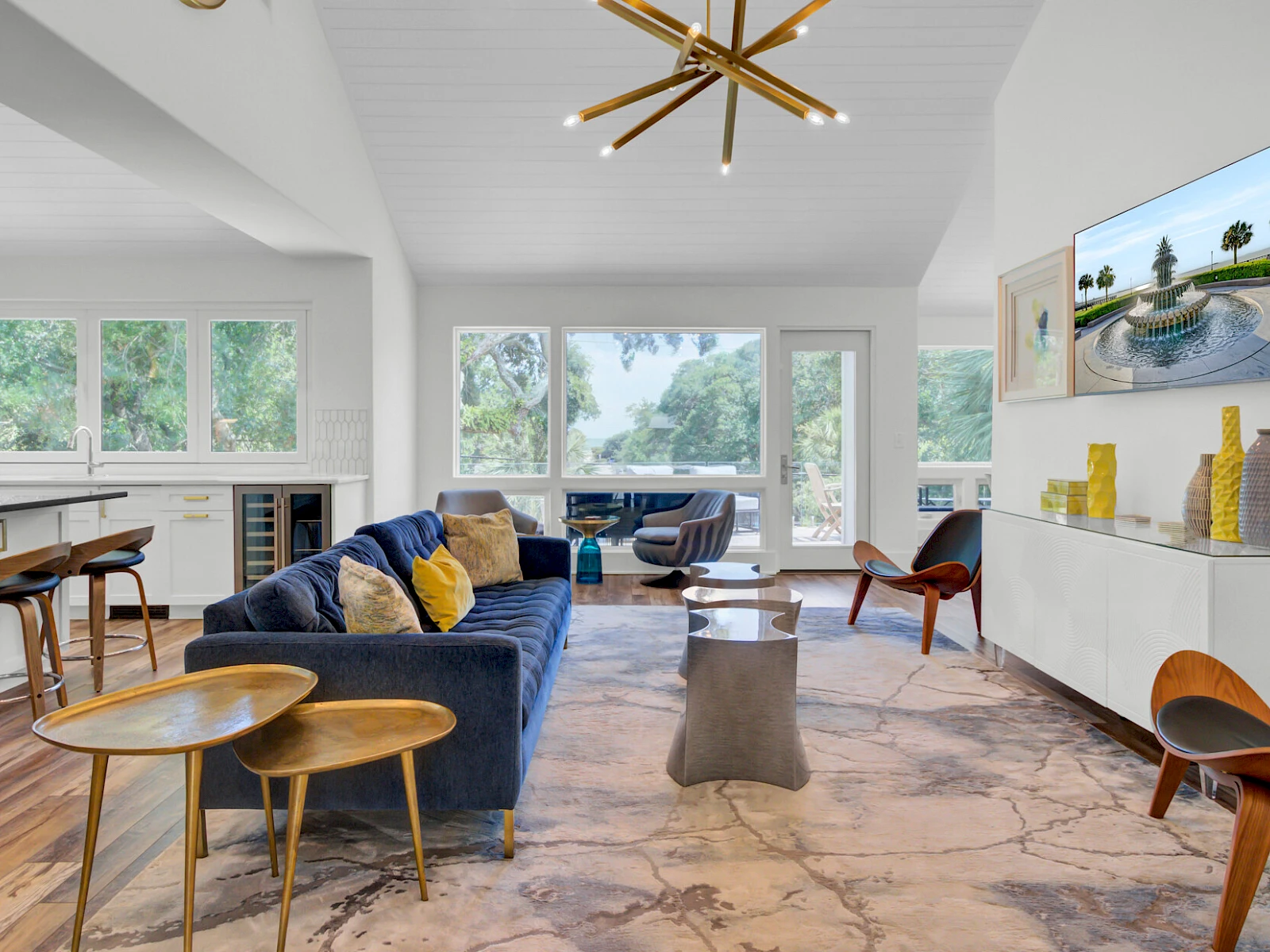 A bright, airy living room with a blue sofa, mid-century chairs, marble floor, large windows, and a wall-mounted TV display; stylish decor and natural light.