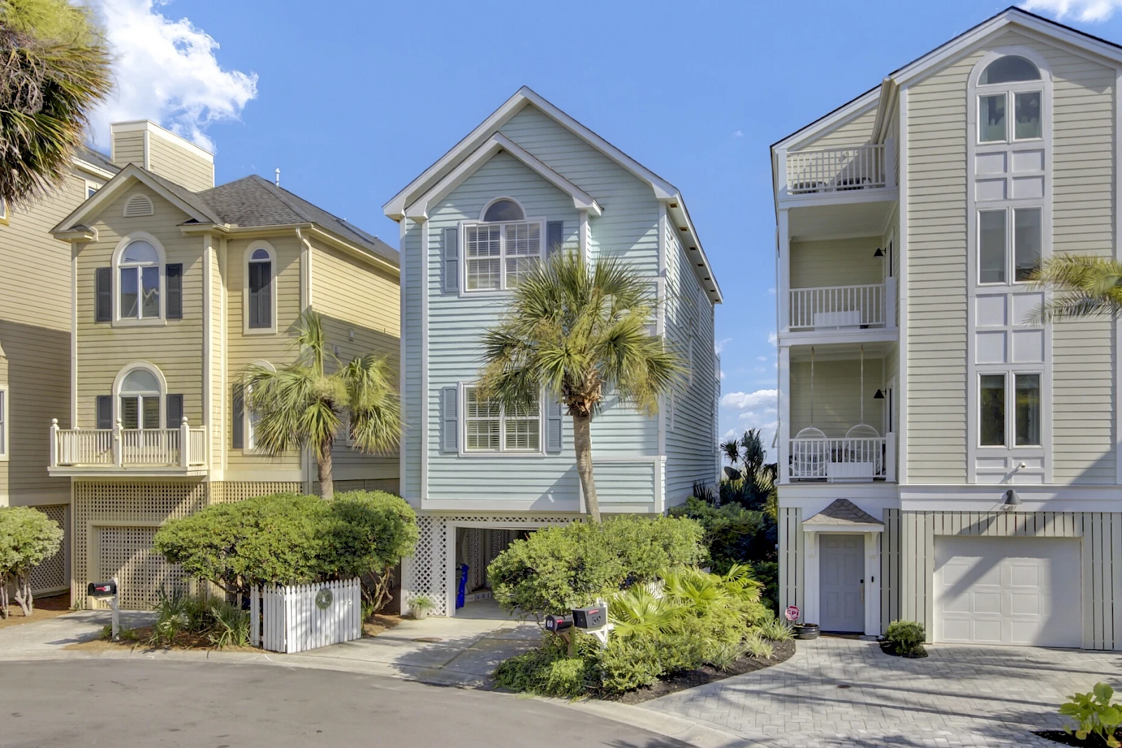 Three colorful coastal houses with palm trees in front, a sunny sky, and a tidy street—vibrant beach neighborhood vibes.