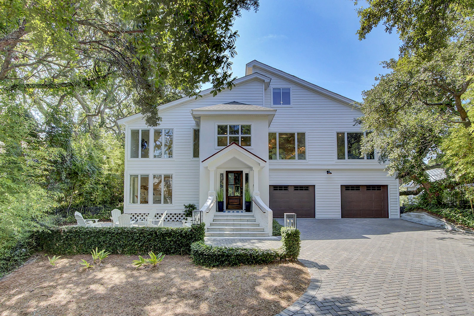 A modern white two-story house with a peaked porch roof, large windows, a dual garage, and a surrounding leafy yard; sunny day backdrop.