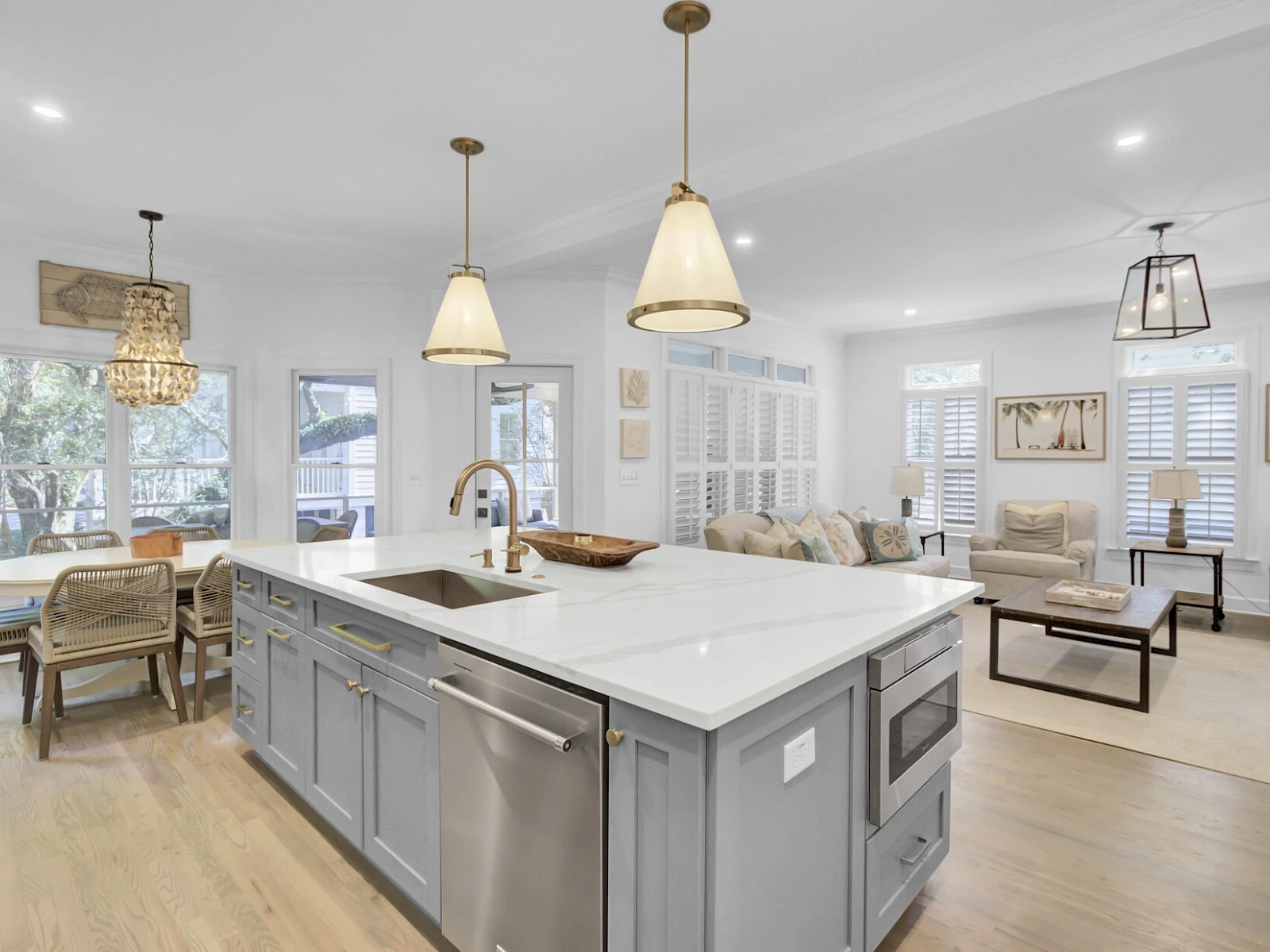Modern open-concept kitchen and living area with a large island, light gray cabinetry, pendant lights, and light wood flooring.