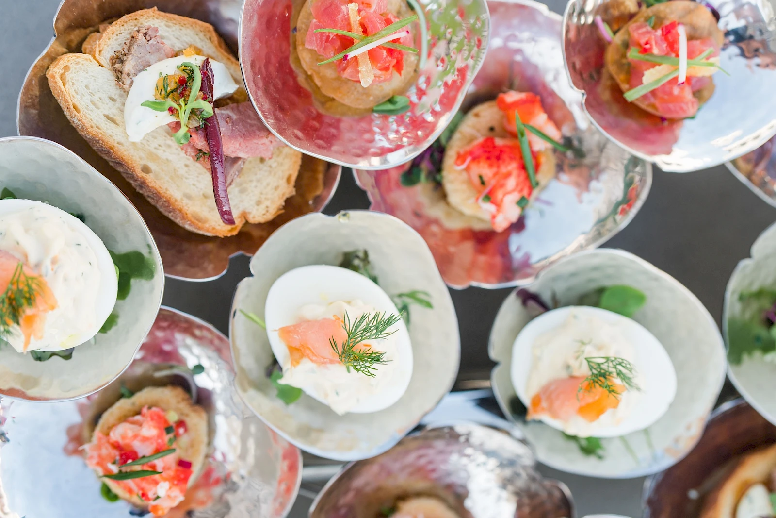 An assortment of elegant canapés: crostini, deviled eggs with herbs, smoked salmon bites, and fresh toppings on stylish glassware, vibrant and bite-sized.