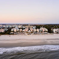 A row of beach houses along a sandy shore with gentle waves, calm sea, and a pastel sky at sunset, peaceful coastal scene.