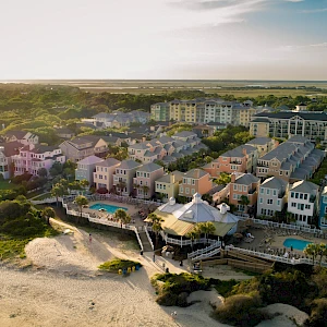 Coastal cliffside town with colorful multi-story beach houses, a row of pools and decks overlooking a sandy shoreline at sunset.