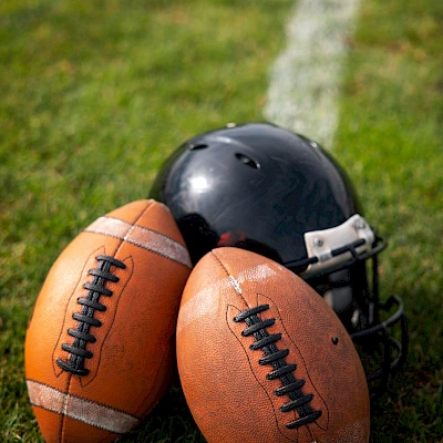 A football (American) and a black helmet resting on grass near the sideline line, bundled together at the edge of the field.