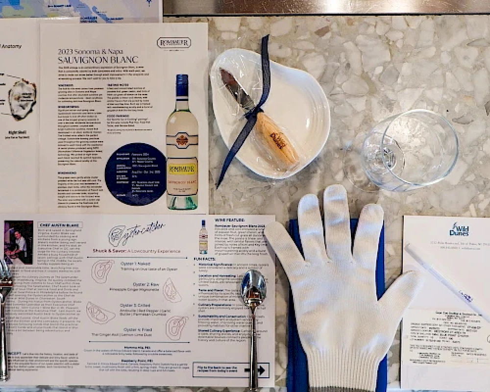 A wine tasting setup with a menu, a bottle of Sauvignon Blanc, a white glove with blue trim, a plate, and cutlery on a marble surface.
