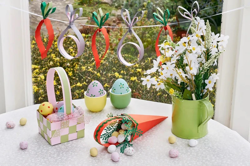 A festive Easter setup: pastel eggs, a basket with small toys, decorative rings hanging above, a bouquet in a green jug, and spring colors. ending with a period.