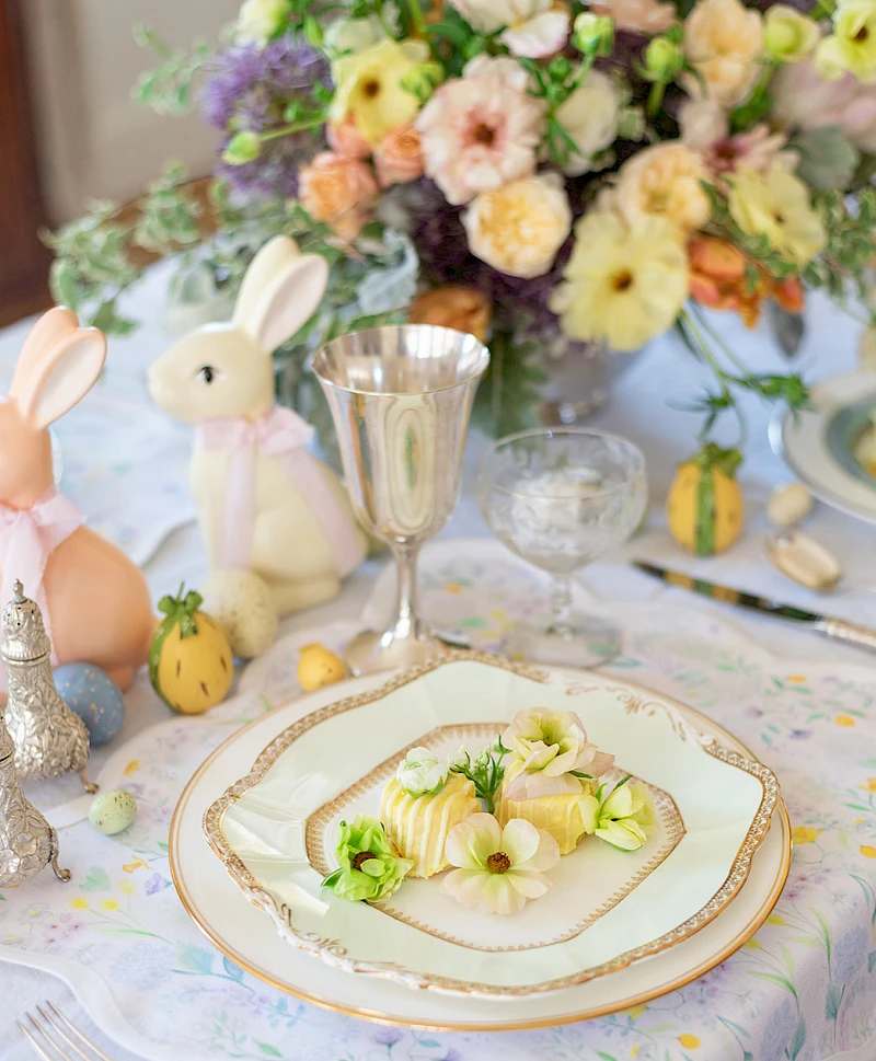 A springtable scene with a floral centerpiece, Easter bunnies, pastel decor, and a plated delicate dish on elegant china, ready for a feast.