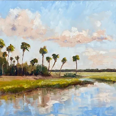 A serene riverbank scene with palm trees, calm water reflecting a blue sky and fluffy clouds, and green marshy banks.