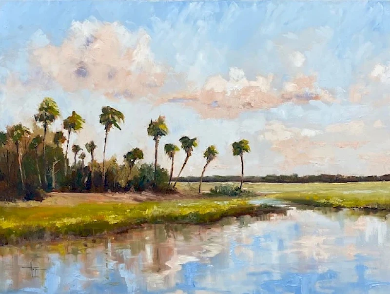 A serene riverbank scene with palm trees, calm water reflecting a blue sky and fluffy clouds, and green marshy banks.