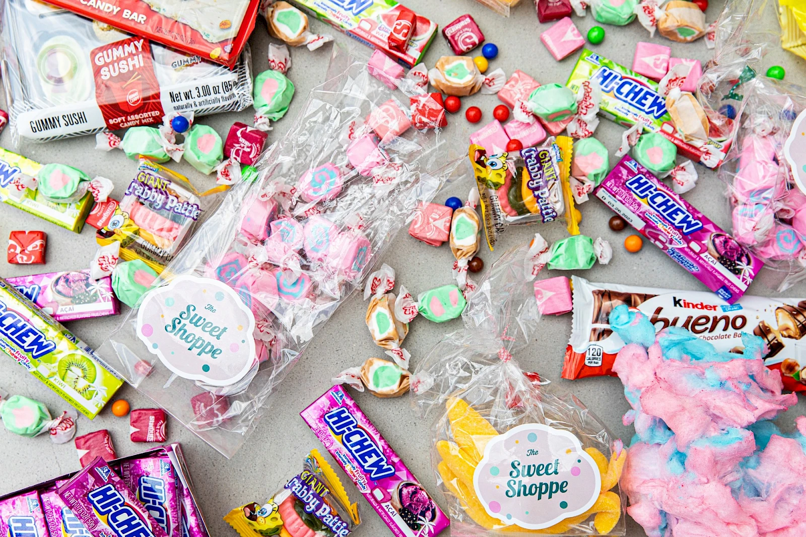 A colorful assortment of candies and sweets scattered on a surface, in wrappers of many brands and pastel shapes, creating a playful candy chaos.
