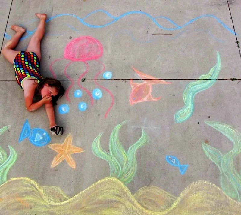 Colorful chalk rainbow on the ground with cups and small flower and heart shapes arranged along its arc.