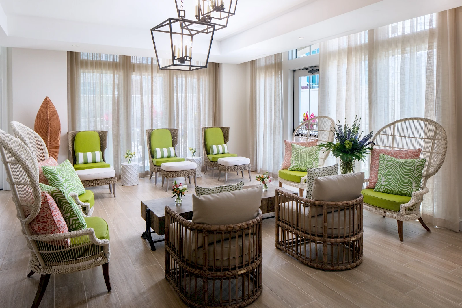 A bright, airy living room with rattan chairs, lime-green cushions, pale curtains, and a circular seating arrangement around a small table. Ends with a period.