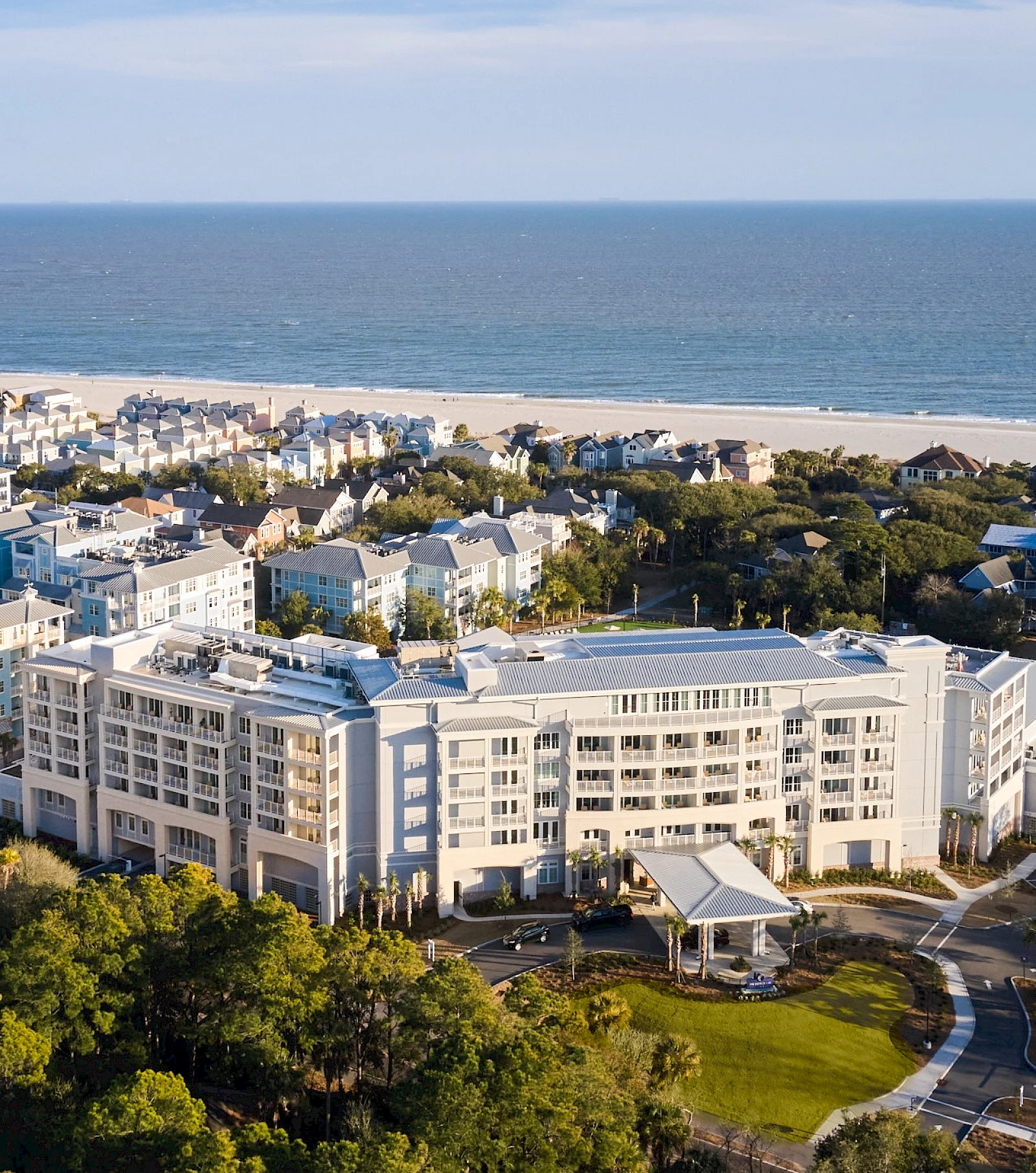 A coastal coastal town with a large white apartment complex, sandy beach, and ocean beyond, surrounded by trees and greenery.