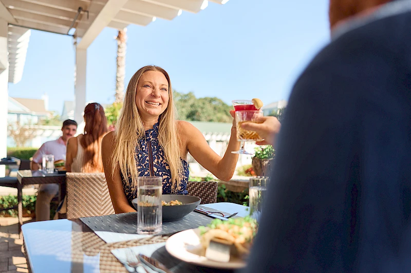 People toasting with drinks outdoors, clinking glasses up toward the sun. Cheers to good times and bright skies.