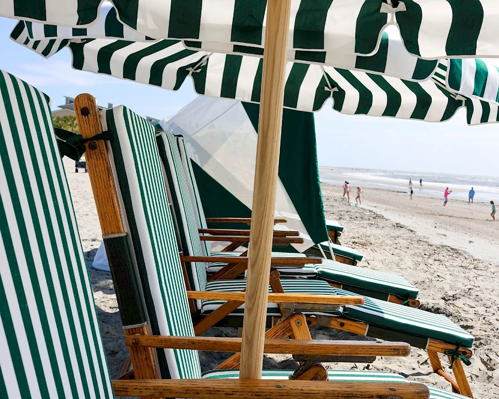 Rows of striped beach chairs under green-and-white umbrellas on a sandy shore, with the sea in the distance.