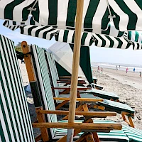Rows of striped beach chairs under green-and-white umbrellas on a sandy shore, with the sea in the distance.
